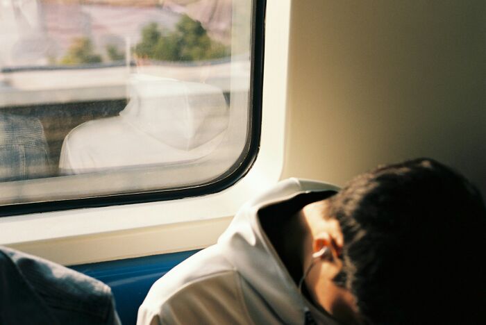 Young man oversleeping on a train, feeling like the worst parent due to repeated oversleeping nightmares.
