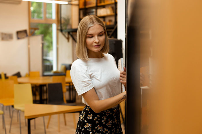 A young woman, likely school office staff, looking at books in a bright room, suggesting secure locking options.
