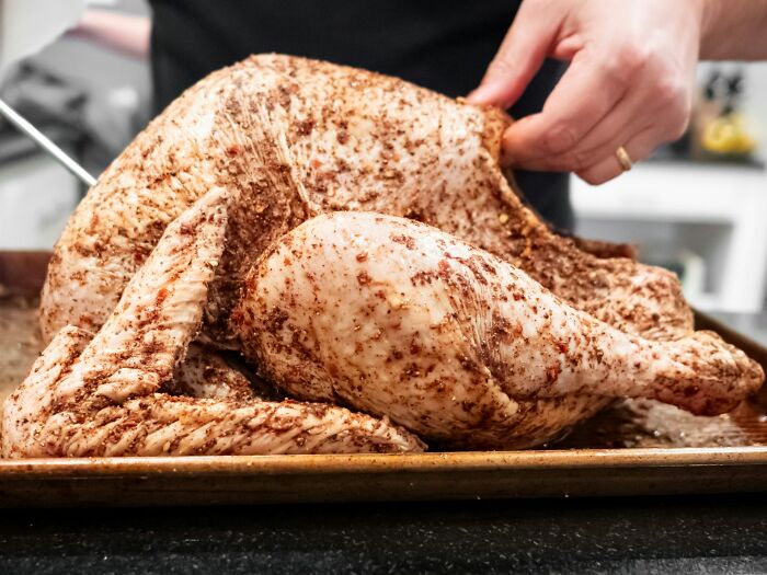 Raw whole chicken seasoned with spices on a baking tray being prepared for cooking in a kitchen setting