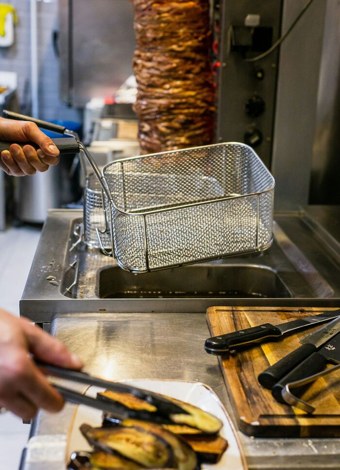 A chef working in a professional kitchen, holding a deep-fry basket, with workplace incidents as a concern.