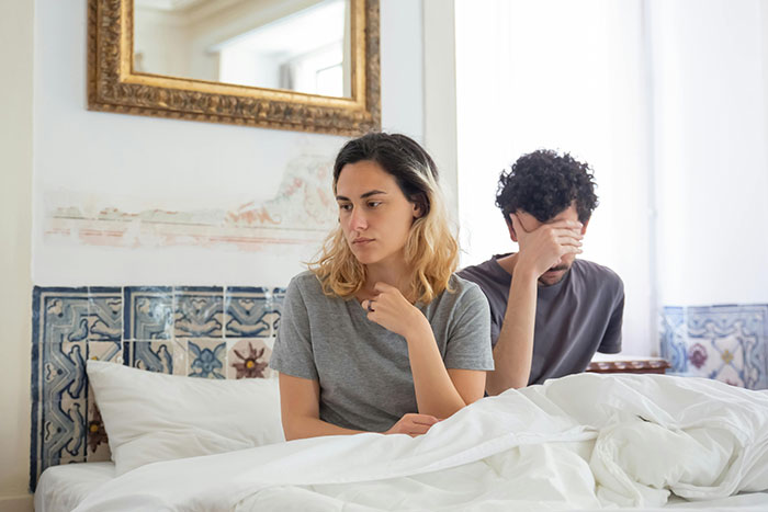 Man ignoring wife, both sitting on a bed with their backs to each other. He has a gut feeling about her coworker.