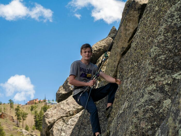 Teen boy rock climbing outdoors on a sunny day illustrating childhood risks and lack of survival instincts.
