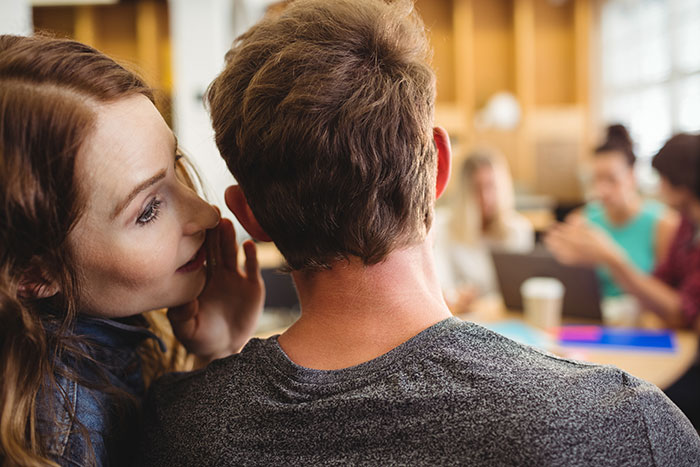 A woman whispers to a man's ear, potentially a toxic bestie sharing secrets or mocking his depression.