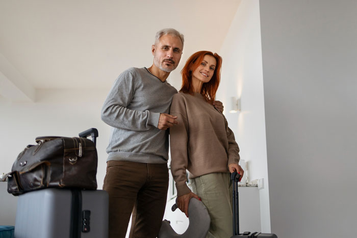 A gray-haired man and a red-haired woman standing with luggage, implying a new life or travel. Keyword: dumps wife.