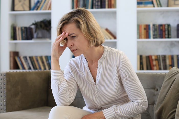 A stressed woman sits on a couch, hand to her forehead, reflecting on how someone could destroy his new life.