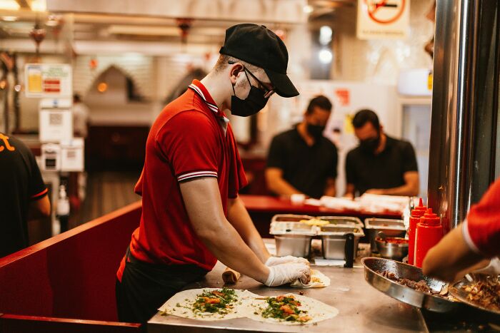 Masked worker in a red shirt and gloves preparing food at a counter. Employers sometimes need to fire someone for various reasons.