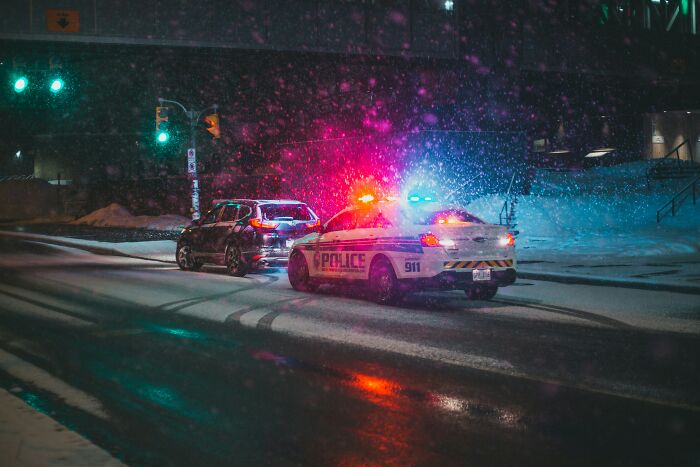 A police car with flashing lights stops another car on a snowy street at night. A situation possibly leading to wildest reasons to fire someone.