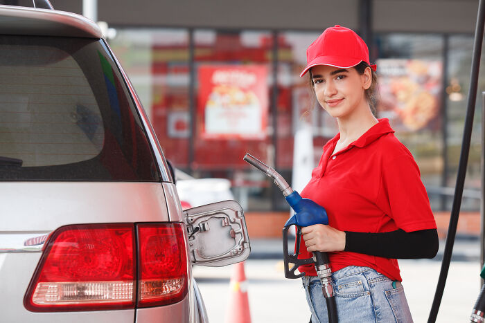 Attendant in red uniform fueling a car. This workplace scene can sometimes include reasons to fire someone.