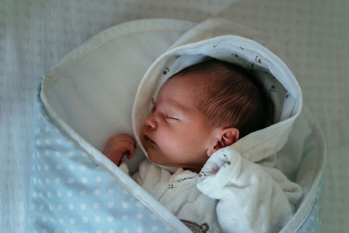 A sleeping newborn baby swaddled in a blue polka dot blanket, peaceful and innocent. Worst MIL stories are far from this calm.