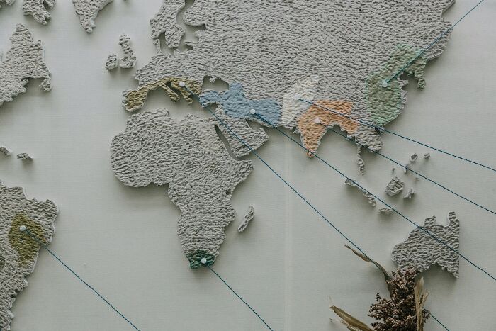 Textured world map with pins & blue strings linking colorful regions in Africa, Europe, & Asia, ideal for World Geography Questions.