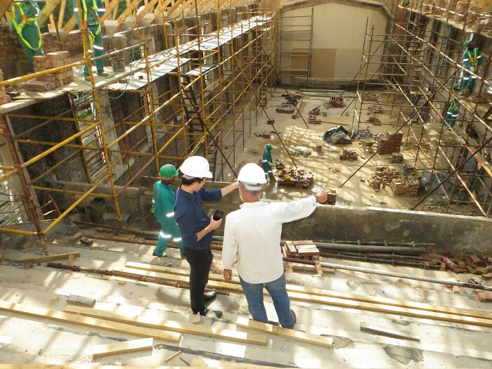 Two supervisors in hard hats at a construction site, pointing at the ongoing work, a moment before someone might rage quit their job.