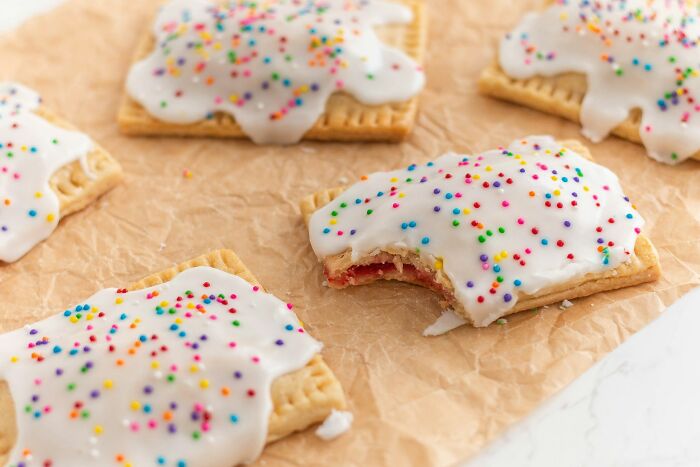 Frosted pastries with colorful sprinkles on parchment paper, a nostalgic family treat now seen as bizarre.