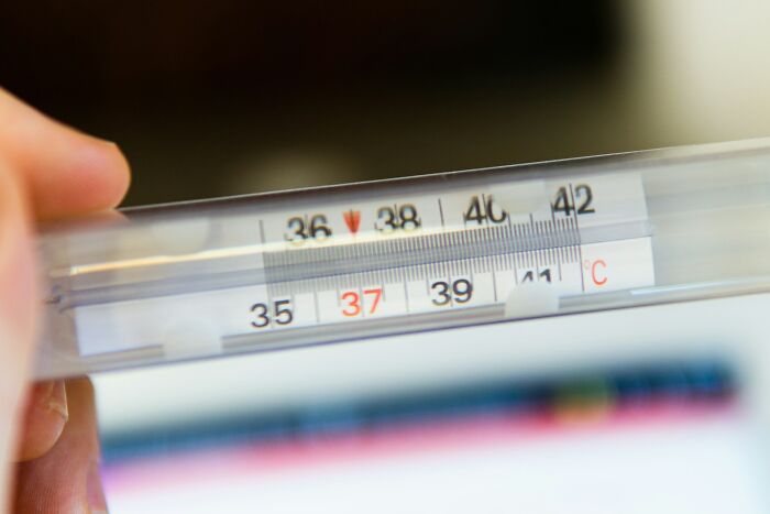 Close-up of a person holding a thermometer showing a temperature near 37 degrees Celsius in a real-life setting.