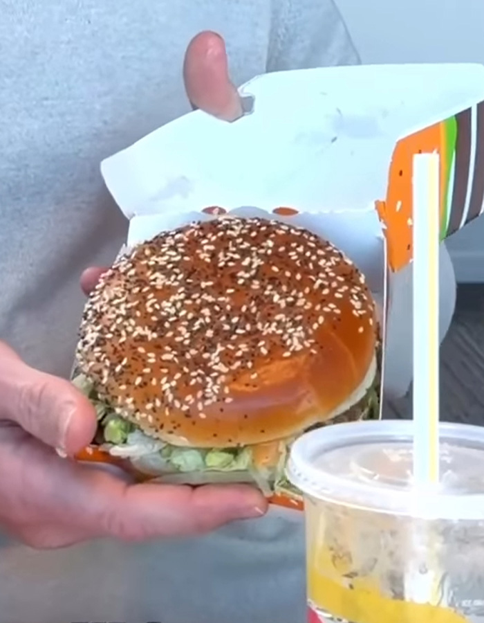 Person holding a Big Arch Burger with sesame seed bun and a drink, related to McDonald&rsquo;s viral reaction discussion.