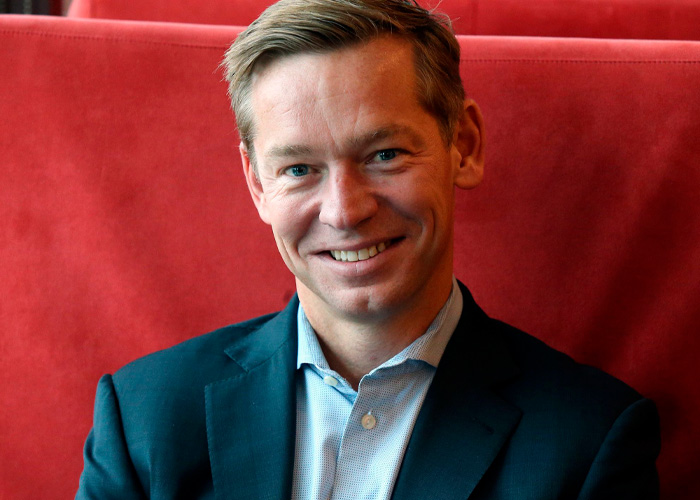Smiling McDonald&rsquo;s CEO in a dark suit sitting against a red background, linked to viral Big Arch Burger reaction discussion.