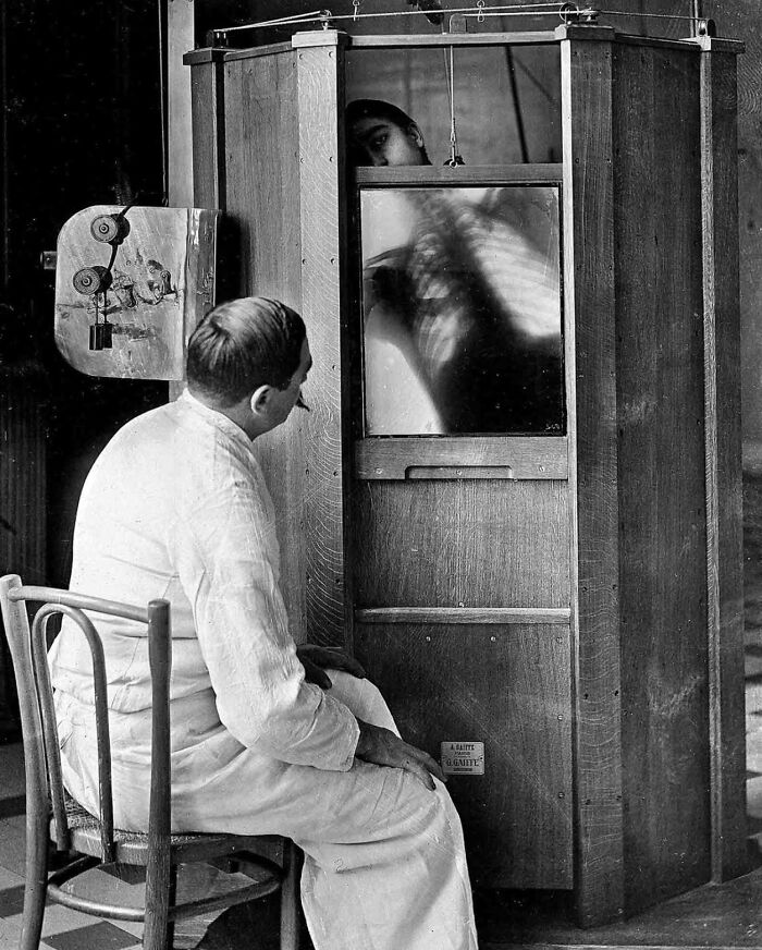 Man in white coat using vintage medical device to view an X-ray, highlighting early medical devices from the past.