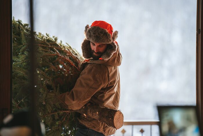 Man in winter coat and hat carrying a Christmas tree, symbolizing adventure and unusual finds in elevator pits.