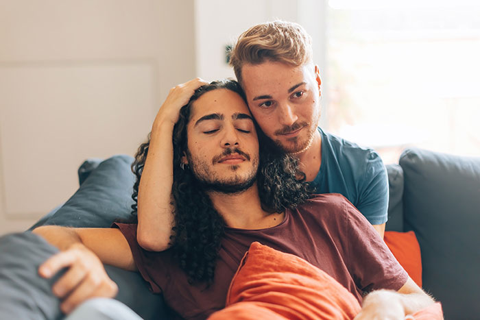 Two men embracing on a couch, representing a loving relationship amidst homophobic tension and police involvement.