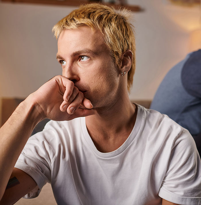 Young man in a white shirt looking worried, reflecting on homophobic MIL trying to get son’s boyfriend arrested.