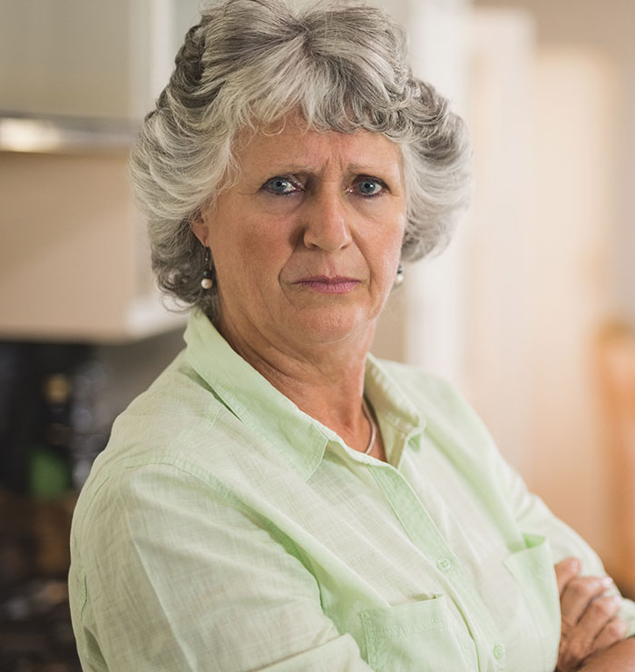 Older woman with gray hair and a serious expression in a light green shirt indoors, representing homophobic MIL tension.