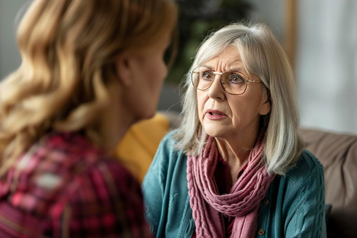 Older woman with glasses looks concerned speaking to another woman, illustrating MIL using emergency key unannounced visit.