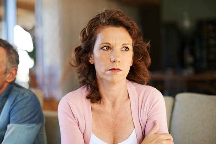 Middle-aged woman looking upset and pensive after MIL uses emergency key to drop in unannounced at family home.