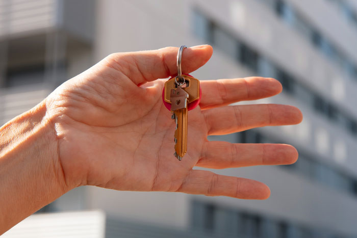 Hand holding a key outside an apartment building, symbolizing emergency key use for unannounced family visits.