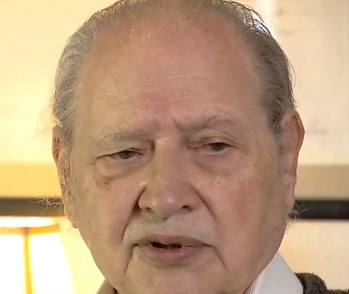 Elderly man speaking in an indoor setting, illustrating historical mistakes with supremely expensive and massive consequences.