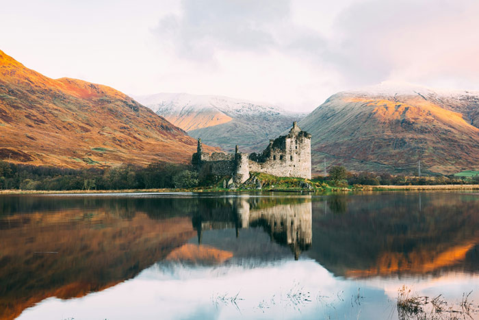 Ruined castle by calm lake with autumn mountains in background symbolizing historical mistakes and consequences.