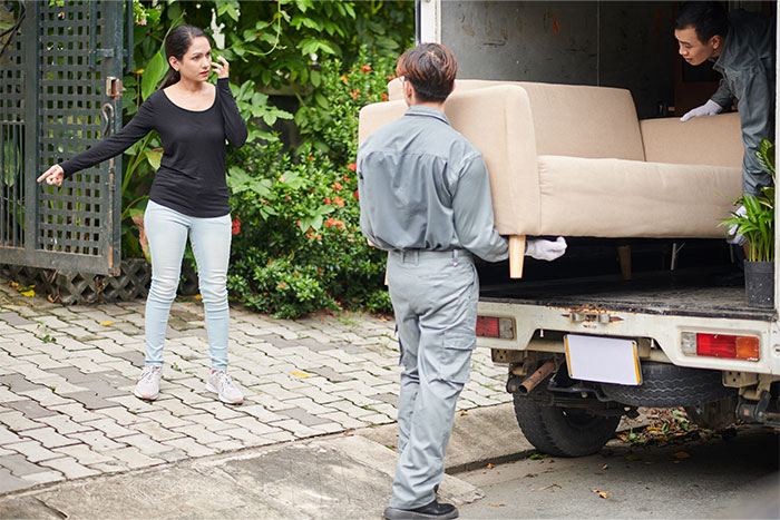 Two men helping a woman load a sofa into a truck, showing support for an overworked and underpaid friend.