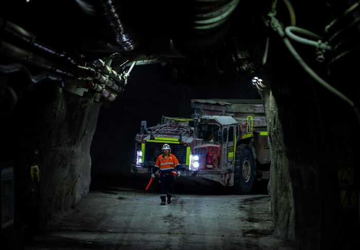 A miner in safety gear walks towards a large mining truck in a dark underground tunnel, a scene that could make someone want to rage quit their jobs.
