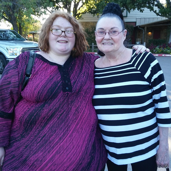 Two women smiling outside, one wearing a purple top and the other in a black and white striped shirt, My 600-Lb. Life star.