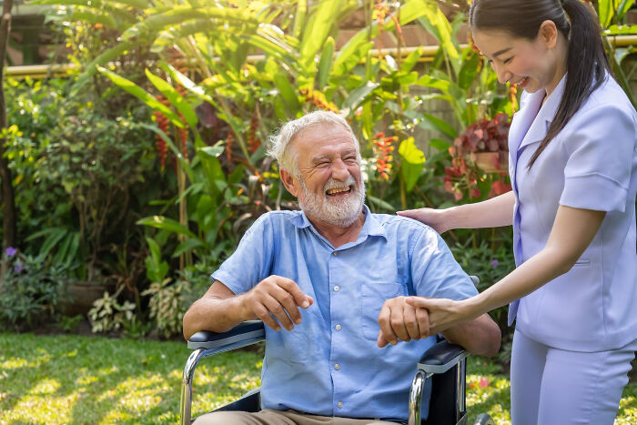 Elderly man in a wheelchair laughs as a female caregiver holds his hand in a garden. This image relates to narcissists.