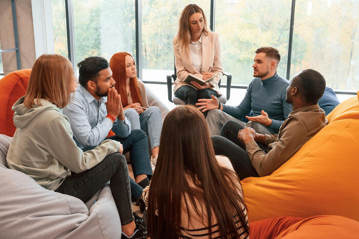 A diverse group sits in a circle for a support meeting, one man talking, others listening intently. Stories of diagnosed narcissists.
