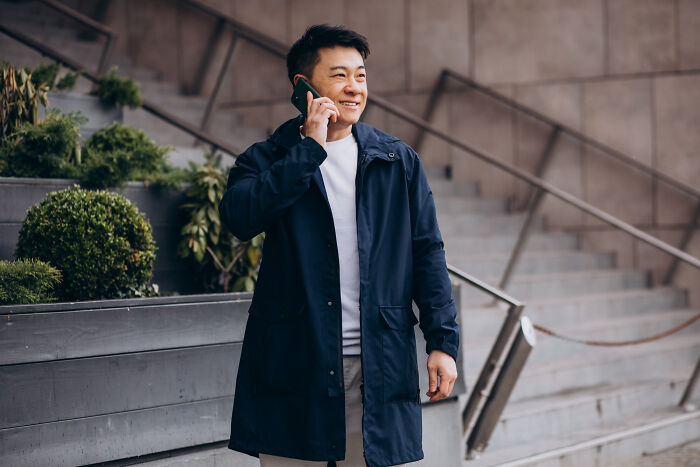 Smiling man in a navy coat on a phone call, standing outside near stairs. These stories prove how narcissists leave a mark.