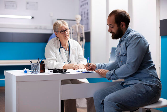 A male patient with a beard filling out forms while a female doctor watches. Diagnosed narcissists leave a mark.