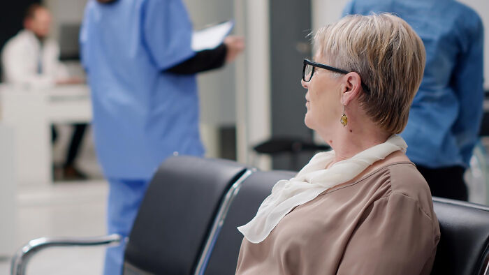 A woman with short blonde hair and glasses sits in a waiting room, reflecting on how diagnosed narcissists leave a mark.