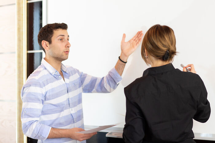 A man in a striped shirt explaining something to a woman writing on a whiteboard, illustrating how narcissists leave a mark.