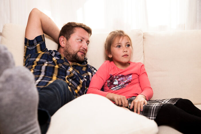 A man and a girl watching TV on a couch, illustrating how narcissists leave a mark on everyone.