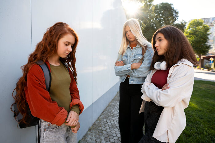 A sad, red-haired girl is ostracized by two frowning girls. This photo illustrates how narcissists leave a mark.