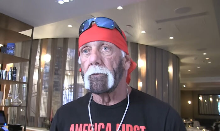 Hulk Hogan wearing a red bandana and sunglasses on his head, a black shirt, and a white beard, symbolizing rudest celebs.
