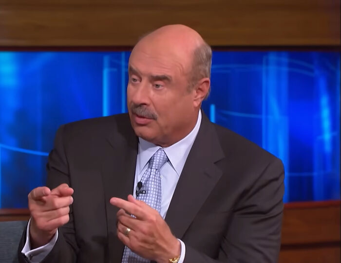 Dr. Phil, a bald man with a mustache, in a suit and tie, pointing, representing some of the rudest celebs.