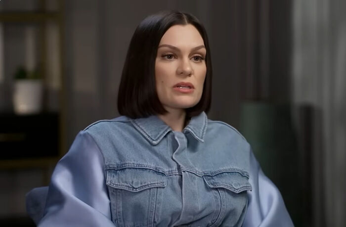 Jessie J, one of the rudest celebs, in a denim jacket with light blue sleeves, looking thoughtful.