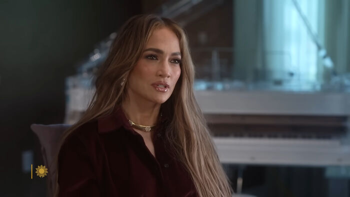 Jennifer Lopez, one of the rudest celebs, with long hair and a gold necklace, appearing pensive in an interview setting.