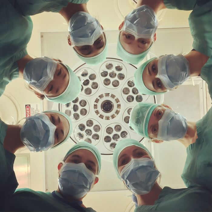 Surgical team wearing masks and scrubs surrounding a bright operating room light, medical facts in action.