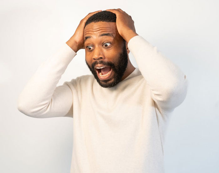 Shocked man in a white sweater holding his head, reacting to an entitled woman damaging his car and ignoring him.