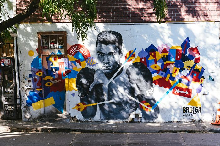 A vibrant mural features a black and white portrait of Muhammad Ali, adorned with colorful abstract art, symbolizing celebrity relatives.
