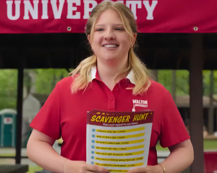 Young woman in a red Walton University shirt holding a scavenger hunt list in Netflix comedy sparking nepotism backlash.