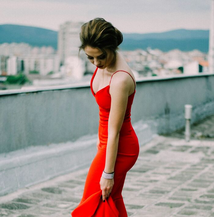 Woman in a red dress standing on a rooftop, looking down with a thoughtful expression, symbolizing weaponized incompetence.