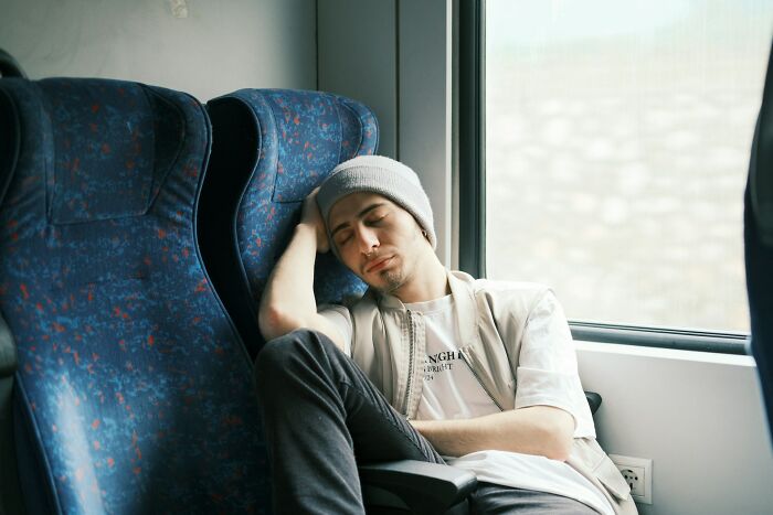 Young man wearing a beanie sleeping on a bus, representing tiredness after wild bachelor and bachelorette parties.
